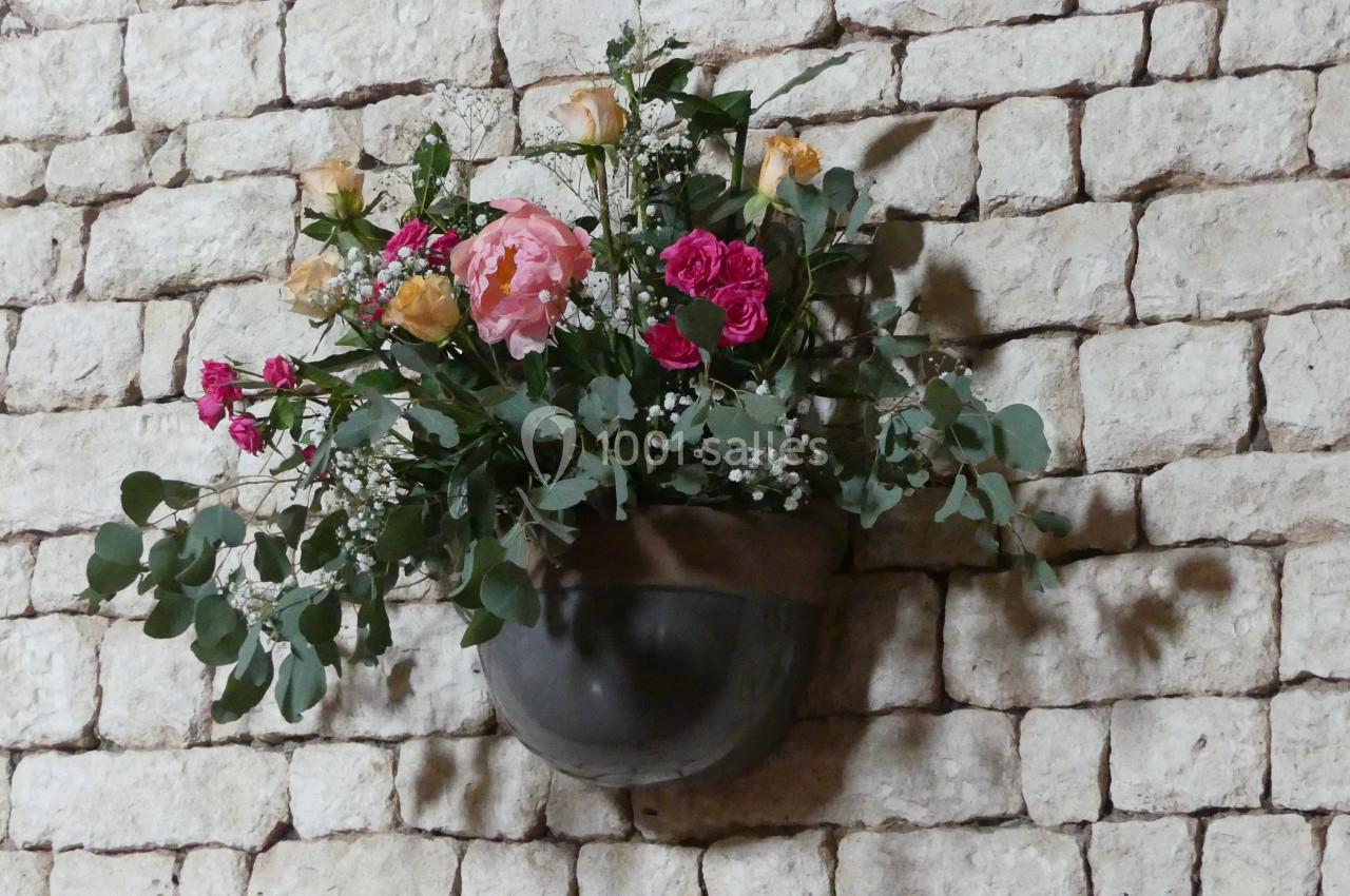 Bouquet de fleurs colorées dans un vase mural en métal, fixé sur un mur en pierre apparente.