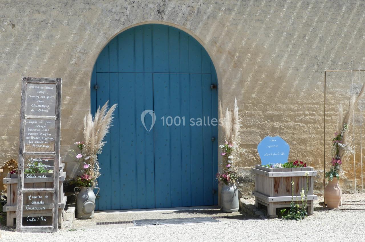 Porte bleue arrondie encadrée de décorations florales et panneaux en bois devant un mur en pierre clair.