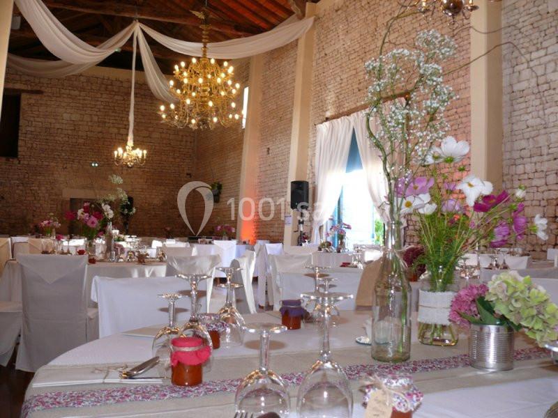 Salle de réception décorée avec des fleurs, nappes blanches et lustres suspendus sous un plafond en bois.