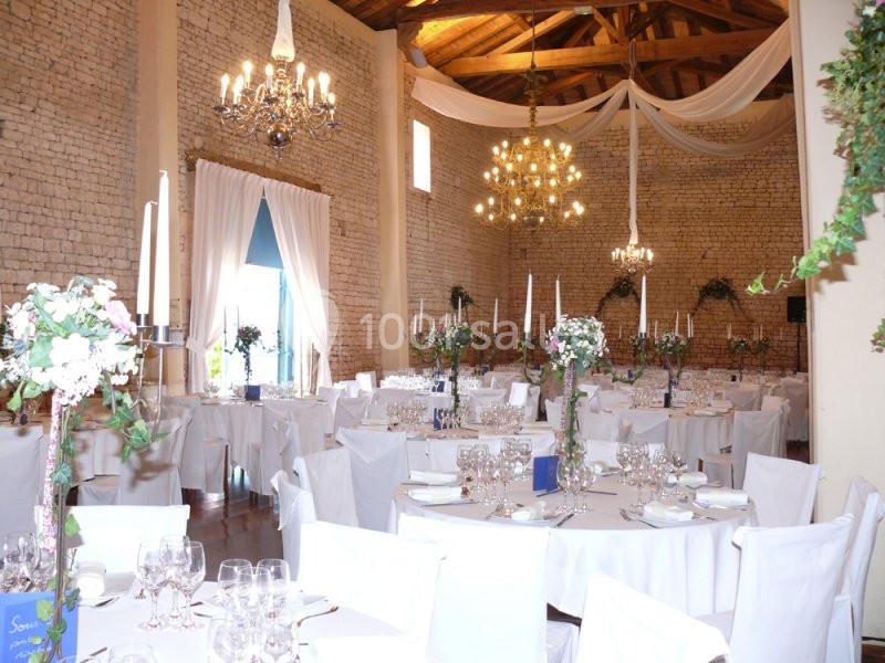 Salle de réception décorée pour un mariage, avec tables dressées, chandeliers et drapés suspendus au plafond.