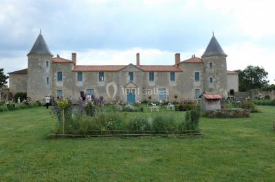 Un couple marche dans le jardin d'un château ancien entouré de verdure par une journée ensoleillée.