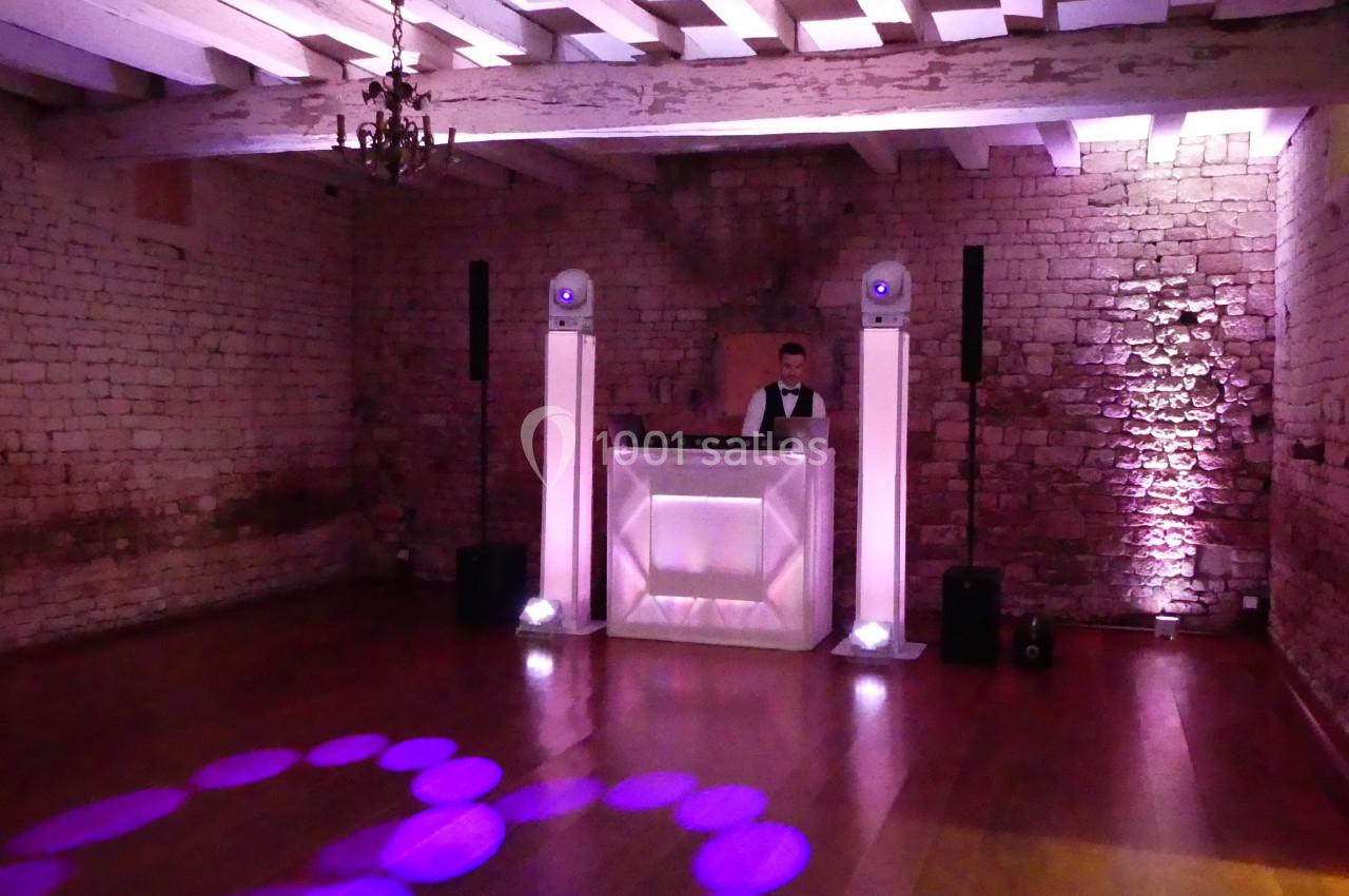 Un DJ derrière une table lumineuse dans une salle en pierre avec éclairage violet et parquet en bois.