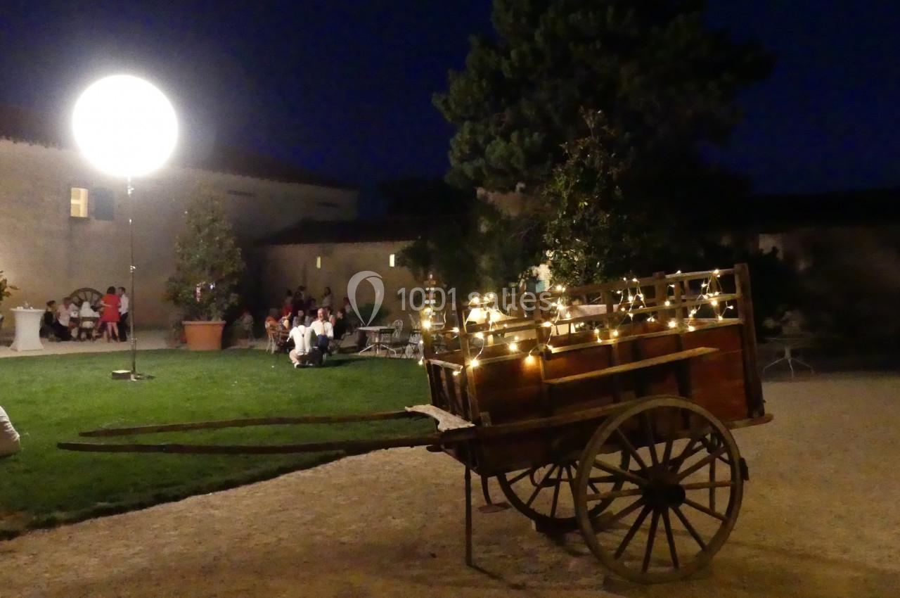 Chariot en bois décoré de guirlandes lumineuses dans une cour éclairée de nuit, avec des personnes en arrière-plan.