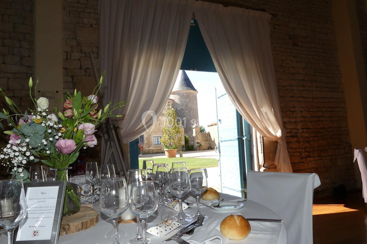 Table dressée avec vaisselle élégante, fleurs et vue sur une cour extérieure avec une tour en arrière-plan.