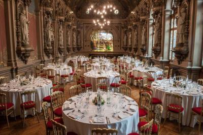 Salle de réception élégante avec tables rondes dressées, décorée de statues, fresques et lustres imposants.