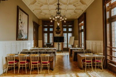 Salle de réception élégante avec tables rondes dressées, décorée de statues, fresques et lustres imposants.