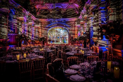 Salle de réception élégante avec tables rondes dressées, décorée de statues, fresques et lustres imposants.