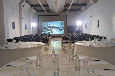 Salle de réception élégante avec tables rondes dressées, décorée de statues, fresques et lustres imposants.