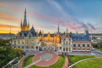 Salle de réception élégante avec tables rondes dressées, décorée de statues, fresques et lustres imposants.