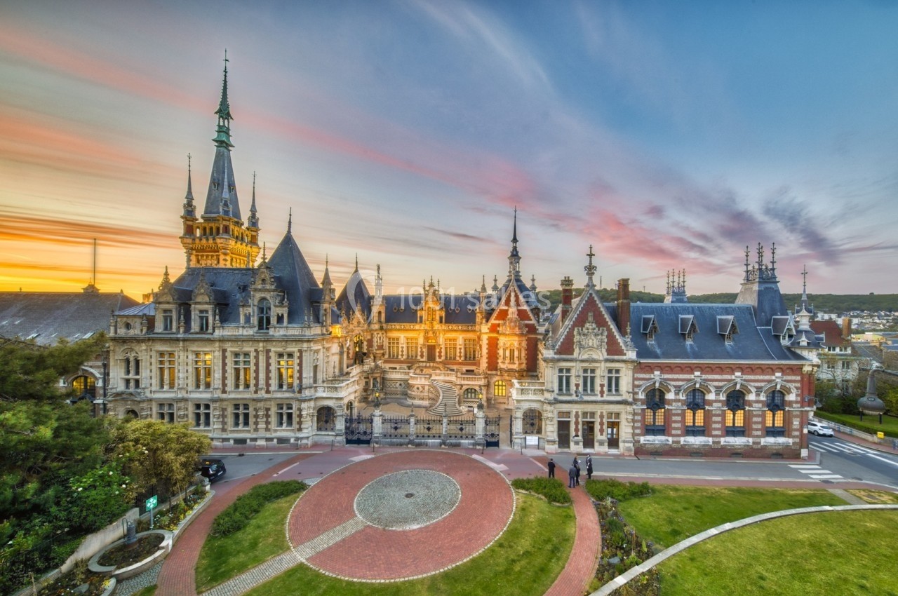 Vue d'un bâtiment historique avec une architecture détaillée, entouré de jardins, au coucher du soleil.