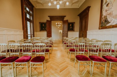Salle de réception élégante avec tables rondes dressées, décorée de statues, fresques et lustres imposants.