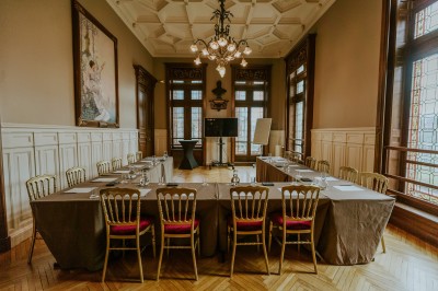 Salle de réception élégante avec tables rondes dressées, décorée de statues, fresques et lustres imposants.