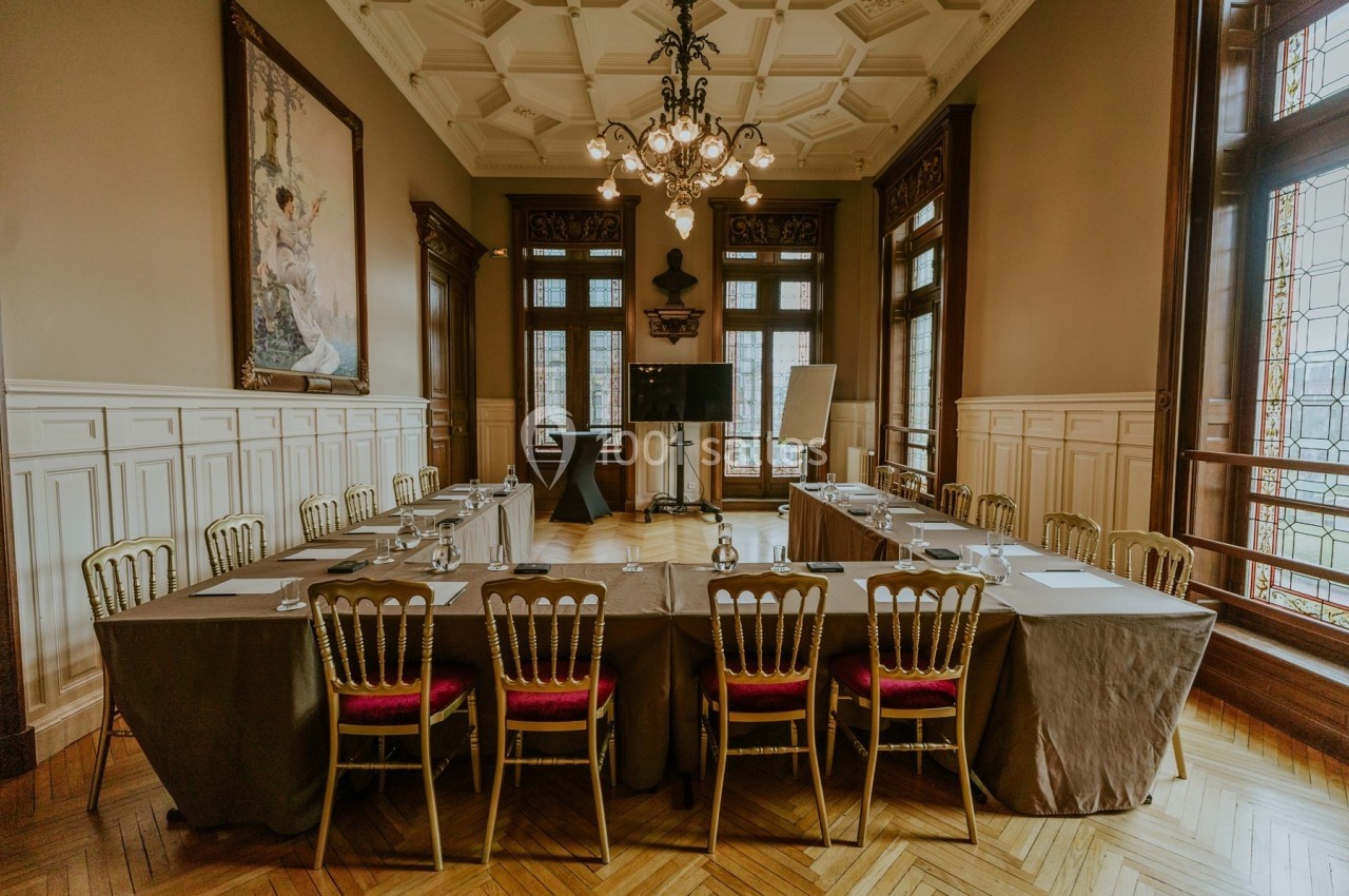 Salle de réunion élégante avec une grande table rectangulaire, chaises dorées et lumière naturelle provenant des fenêtres.