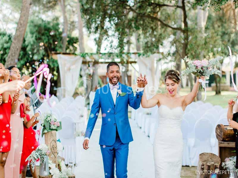 Un couple souriant marche main dans la main lors de leur cérémonie de mariage en plein air, entouré d'invités.