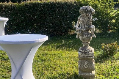 Salle avec un ancien pressoir en bois, des tonneaux, une table rouge avec bouteilles et des verres à vin.