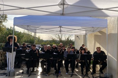 Salle avec un ancien pressoir en bois, des tonneaux, une table rouge avec bouteilles et des verres à vin.