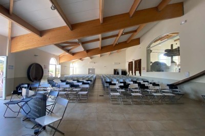 Salle avec un ancien pressoir en bois, des tonneaux, une table rouge avec bouteilles et des verres à vin.