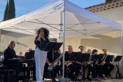 Salle avec un ancien pressoir en bois, des tonneaux, une table rouge avec bouteilles et des verres à vin.