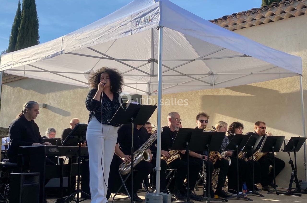 Chanteuse interprétant une chanson sur scène, accompagnée d'un orchestre sous une tente blanche en extérieur.