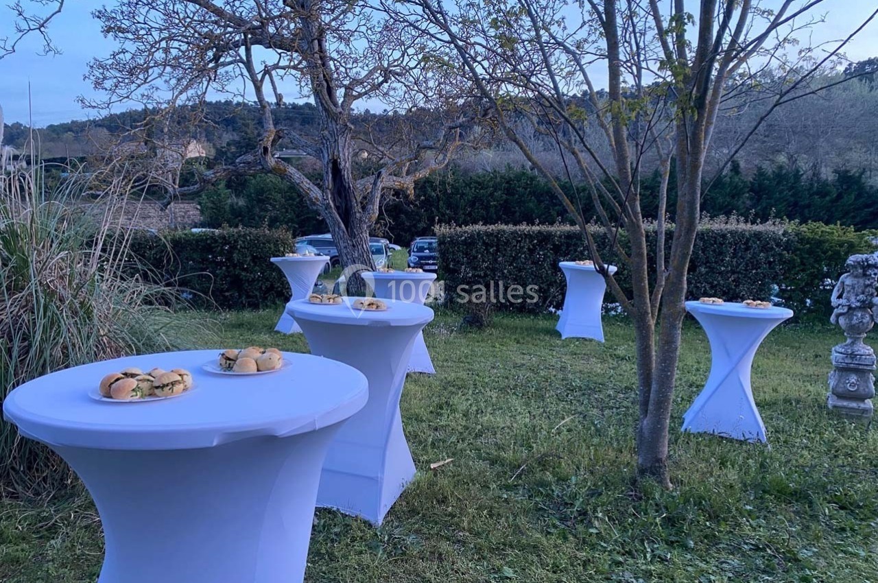Tables hautes blanches dressées avec des plateaux de sandwichs dans un jardin au crépuscule.
