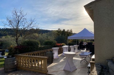 Salle avec un ancien pressoir en bois, des tonneaux, une table rouge avec bouteilles et des verres à vin.