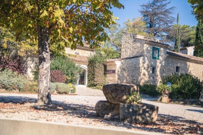 Salle avec un ancien pressoir en bois, des tonneaux, une table rouge avec bouteilles et des verres à vin.