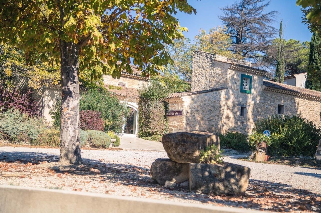 Cour d'une maison en pierre entourée de végétation, avec des arbres aux feuilles automnales et des pierres empilées au…