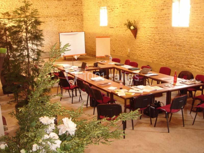 Salle de réunion avec tables disposées en U, chaises rouges, paperboards et décorations végétales.