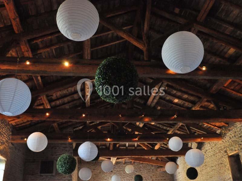 Plafond en bois avec des lanternes blanches suspendues et des sphères végétales dans une salle en pierre.