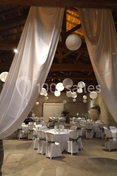 Salle de réception décorée avec des drapés blancs, des lanternes suspendues et des tables dressées pour un événement.