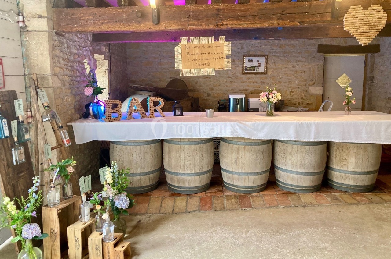 Comptoir de bar rustique décoré de fleurs, caisses en bois et lettres lumineuses, installé sur des tonneaux en bois.