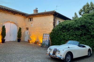 Table en bois avec des objets décoratifs, posée contre un mur en pierre dans une pièce lumineuse au sol en terre cuite.