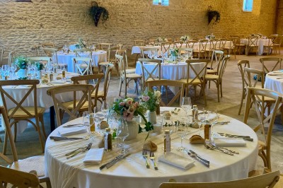 Table en bois avec des objets décoratifs, posée contre un mur en pierre dans une pièce lumineuse au sol en terre cuite.