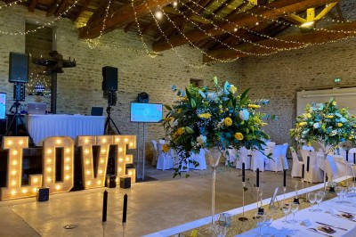 Table en bois avec des objets décoratifs, posée contre un mur en pierre dans une pièce lumineuse au sol en terre cuite.