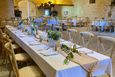 Table en bois avec des objets décoratifs, posée contre un mur en pierre dans une pièce lumineuse au sol en terre cuite.