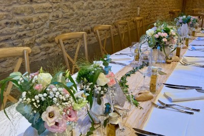 Table en bois avec des objets décoratifs, posée contre un mur en pierre dans une pièce lumineuse au sol en terre cuite.