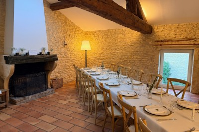 Table en bois avec des objets décoratifs, posée contre un mur en pierre dans une pièce lumineuse au sol en terre cuite.