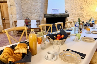 Table en bois avec des objets décoratifs, posée contre un mur en pierre dans une pièce lumineuse au sol en terre cuite.