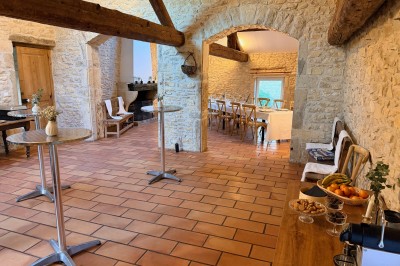Table en bois avec des objets décoratifs, posée contre un mur en pierre dans une pièce lumineuse au sol en terre cuite.