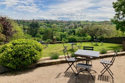 Table en bois avec des objets décoratifs, posée contre un mur en pierre dans une pièce lumineuse au sol en terre cuite.