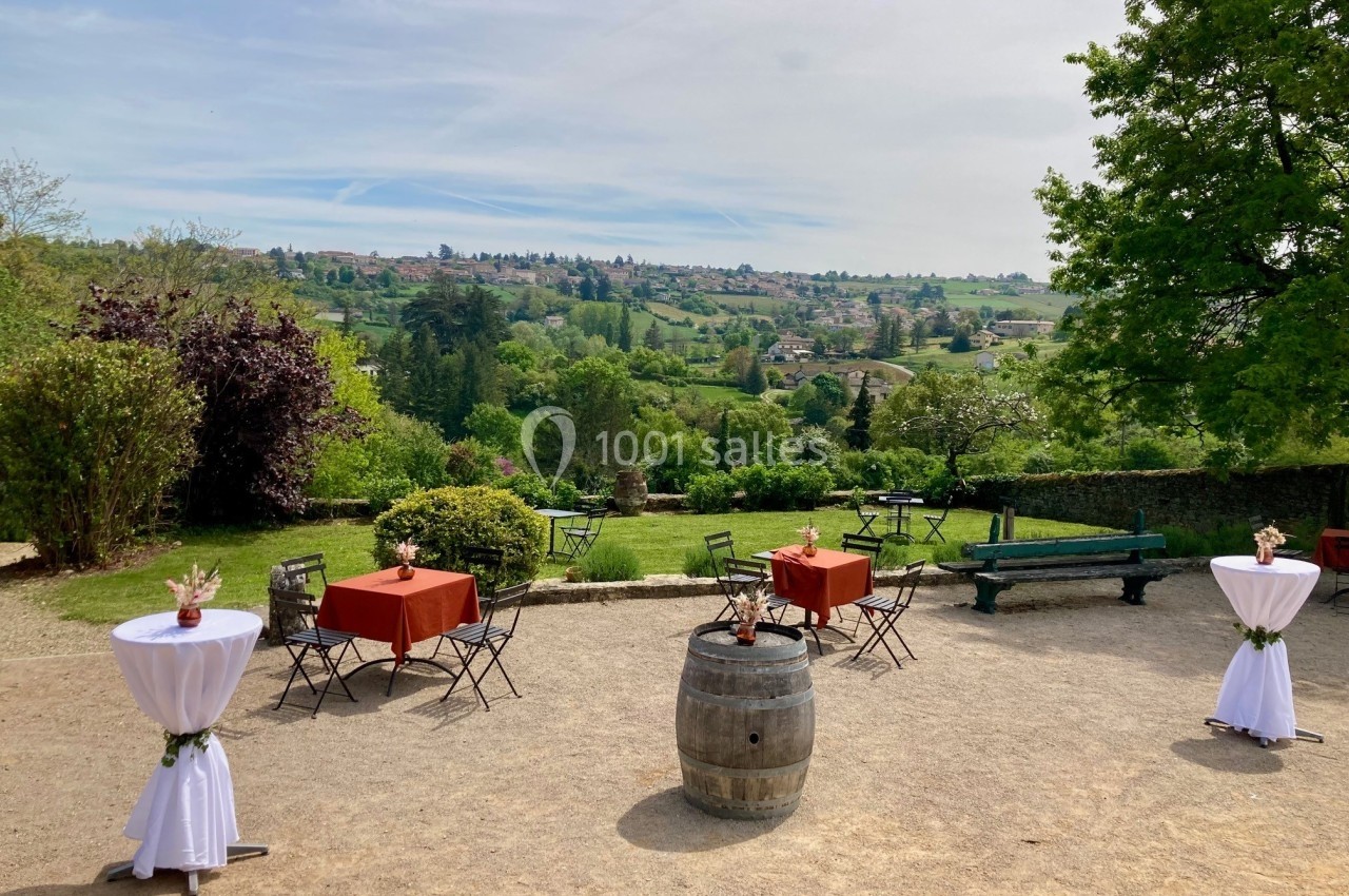 Terrasse extérieure avec tables et chaises, vue sur un paysage verdoyant et vallonné sous un ciel dégagé.