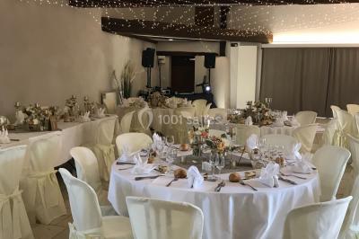 Petit pont en fer forgé traversant un cours d'eau bordé d'arbres, près d'une maison en pierre avec toit en ardoise.