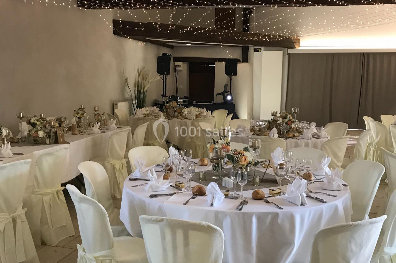 Salle de réception décorée avec des tables rondes dressées, nappes blanches et guirlandes lumineuses suspendues.