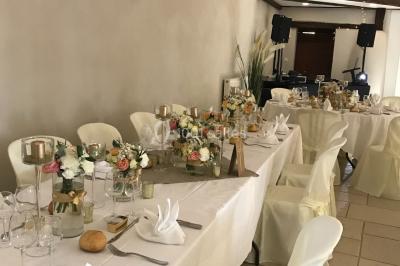 Petit pont en fer forgé traversant un cours d'eau bordé d'arbres, près d'une maison en pierre avec toit en ardoise.