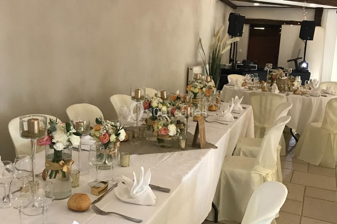 Salle de réception décorée avec des tables dressées, nappes blanches, arrangements floraux et guirlandes lumineuses…