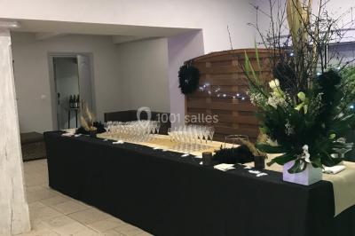 Petit pont en fer forgé traversant un cours d'eau bordé d'arbres, près d'une maison en pierre avec toit en ardoise.