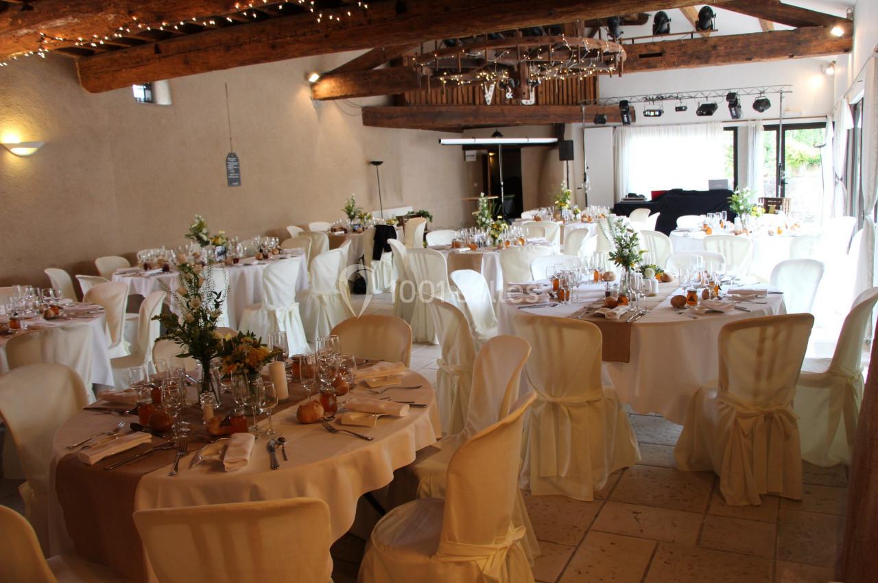 Salle de réception décorée avec des tables rondes dressées, nappes blanches et arrangements floraux.