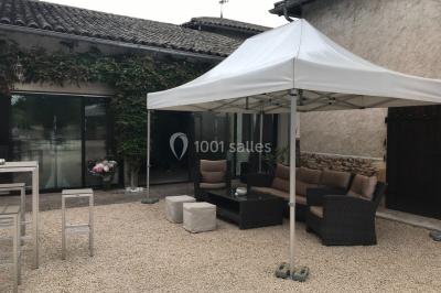 Petit pont en fer forgé traversant un cours d'eau bordé d'arbres, près d'une maison en pierre avec toit en ardoise.