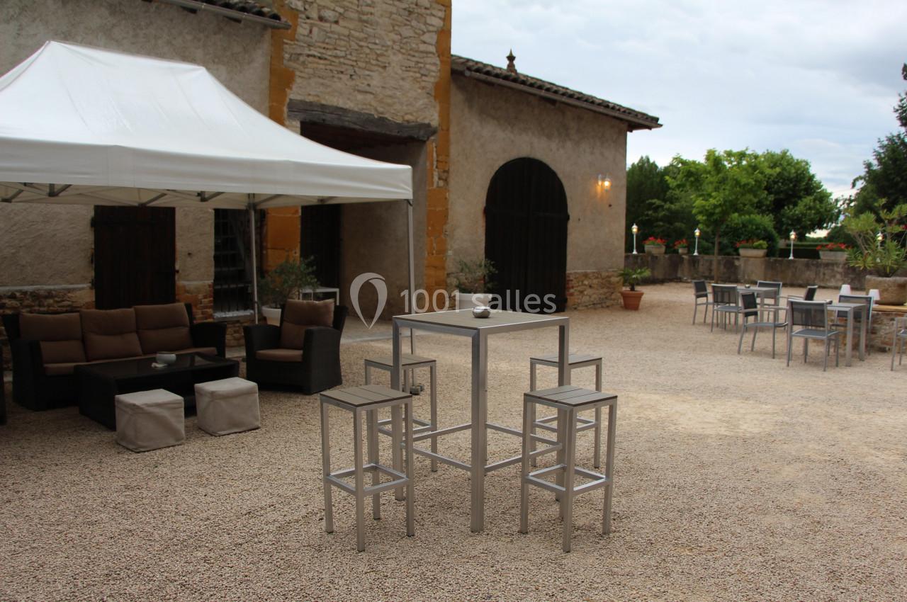 Cour avec mobilier de jardin moderne, comprenant un canapé sous un barnum blanc et des tables hautes avec chaises.
