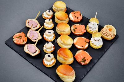 Petit pont en fer forgé traversant un cours d'eau bordé d'arbres, près d'une maison en pierre avec toit en ardoise.
